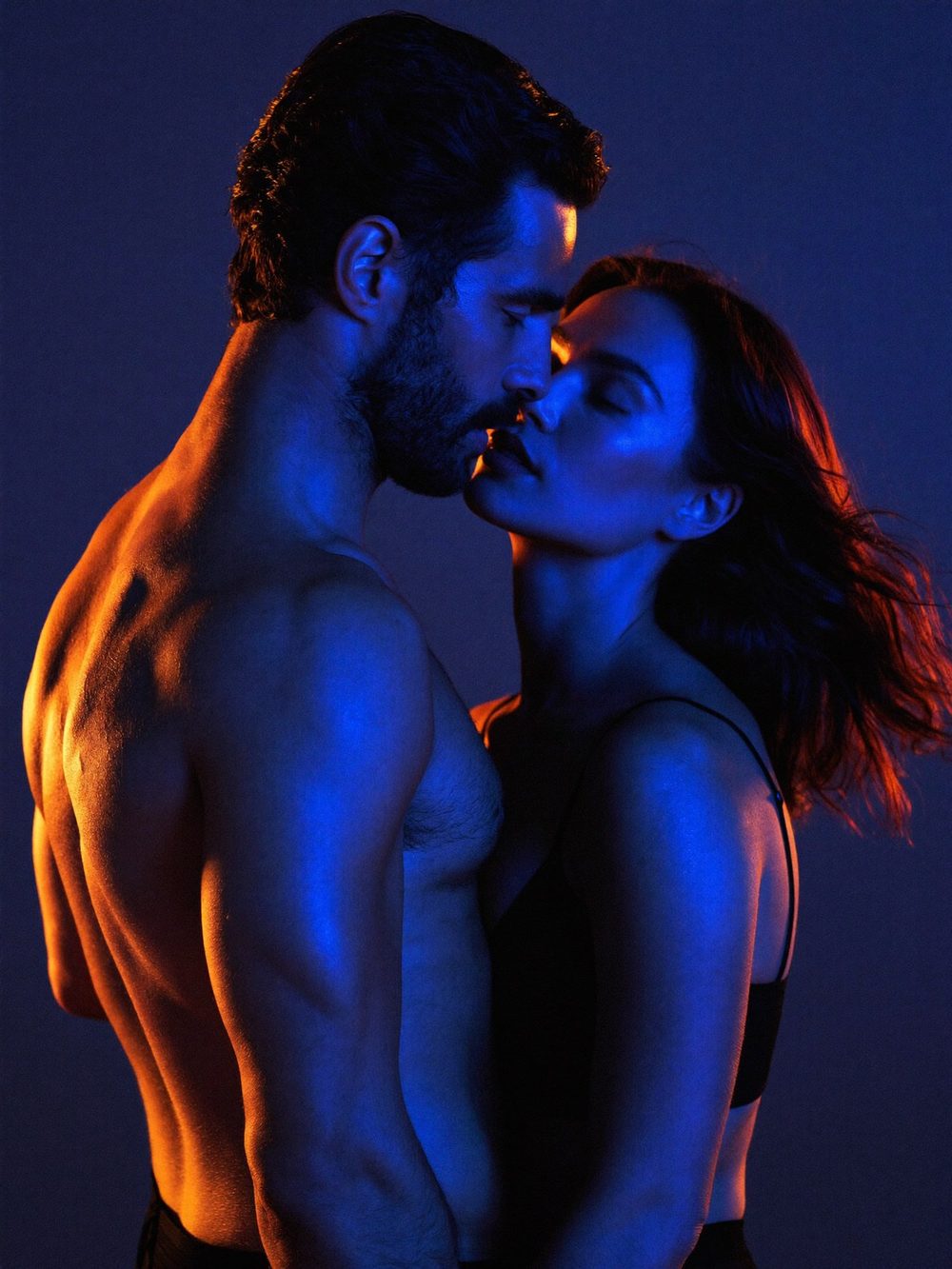 A confident man in an open black shirt under blue light