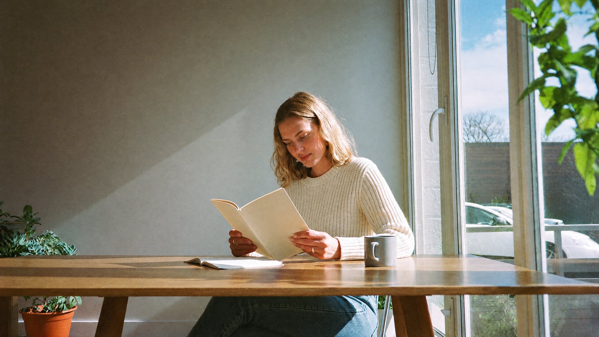 A woman reading at a sunny kitchen table