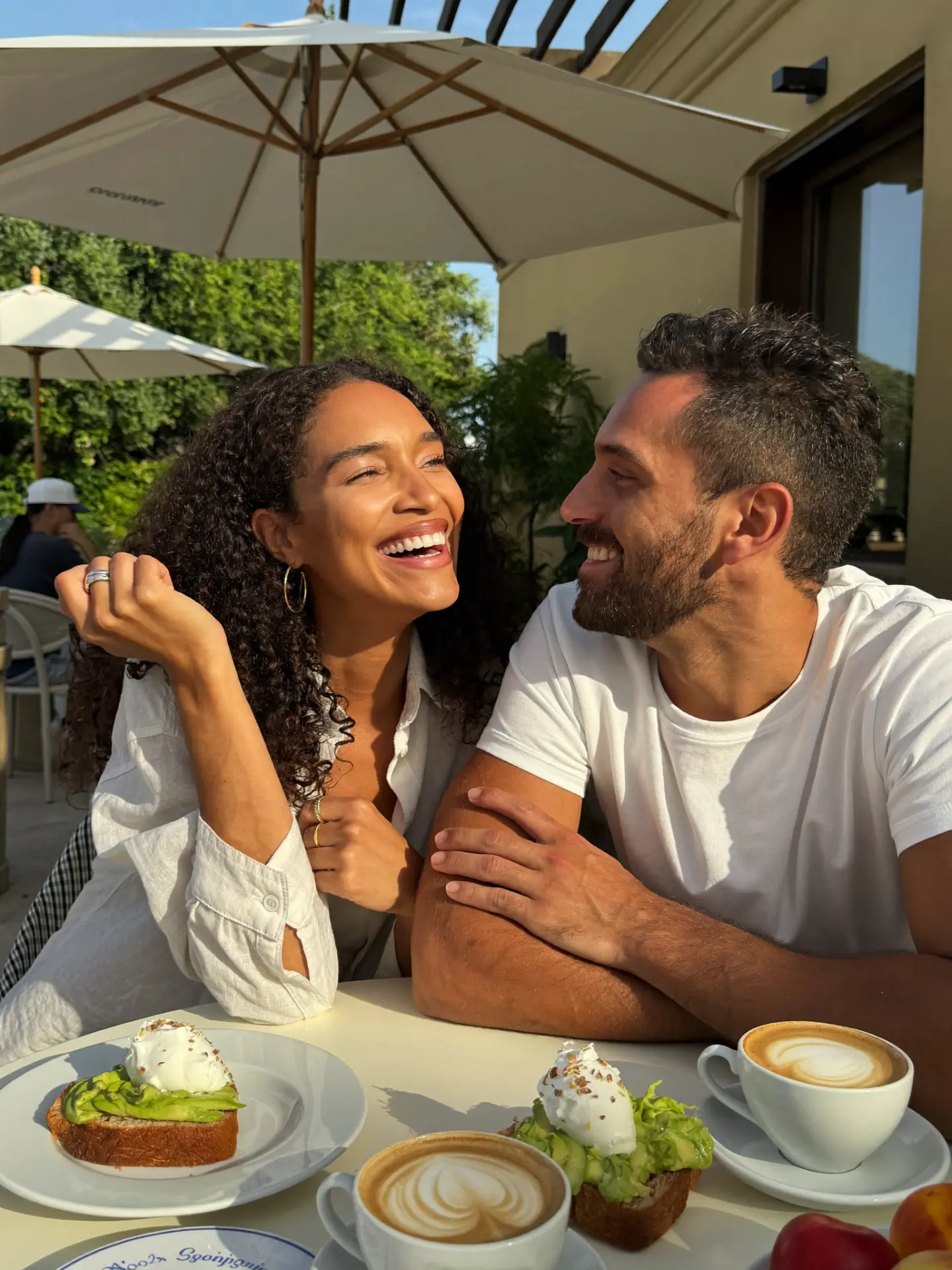 A couple laughing over brunch at a sunlit outdoor café
