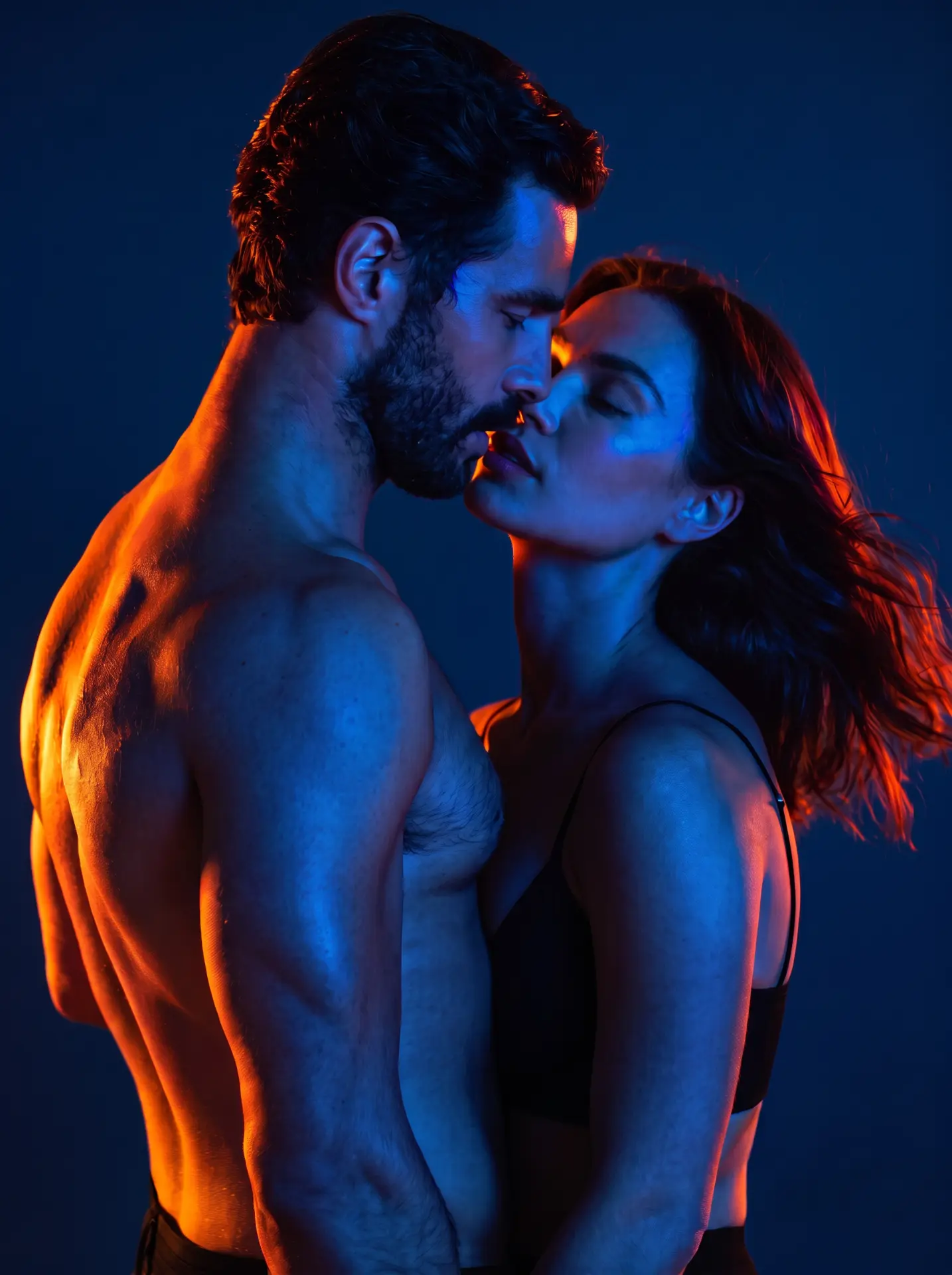 A bearded man leaning in to kiss a woman in a close embrace, both with their eyes closed, lit in deep blue with warm orange rim light