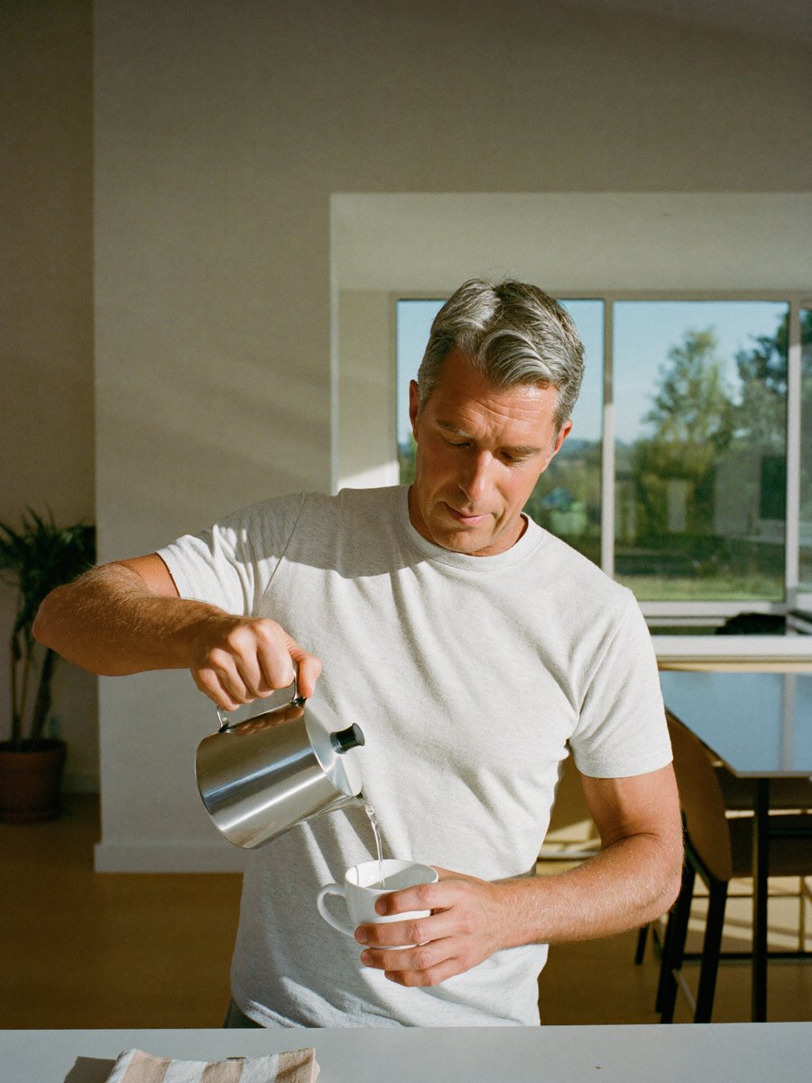A man making pour-over coffee in a sunny kitchen